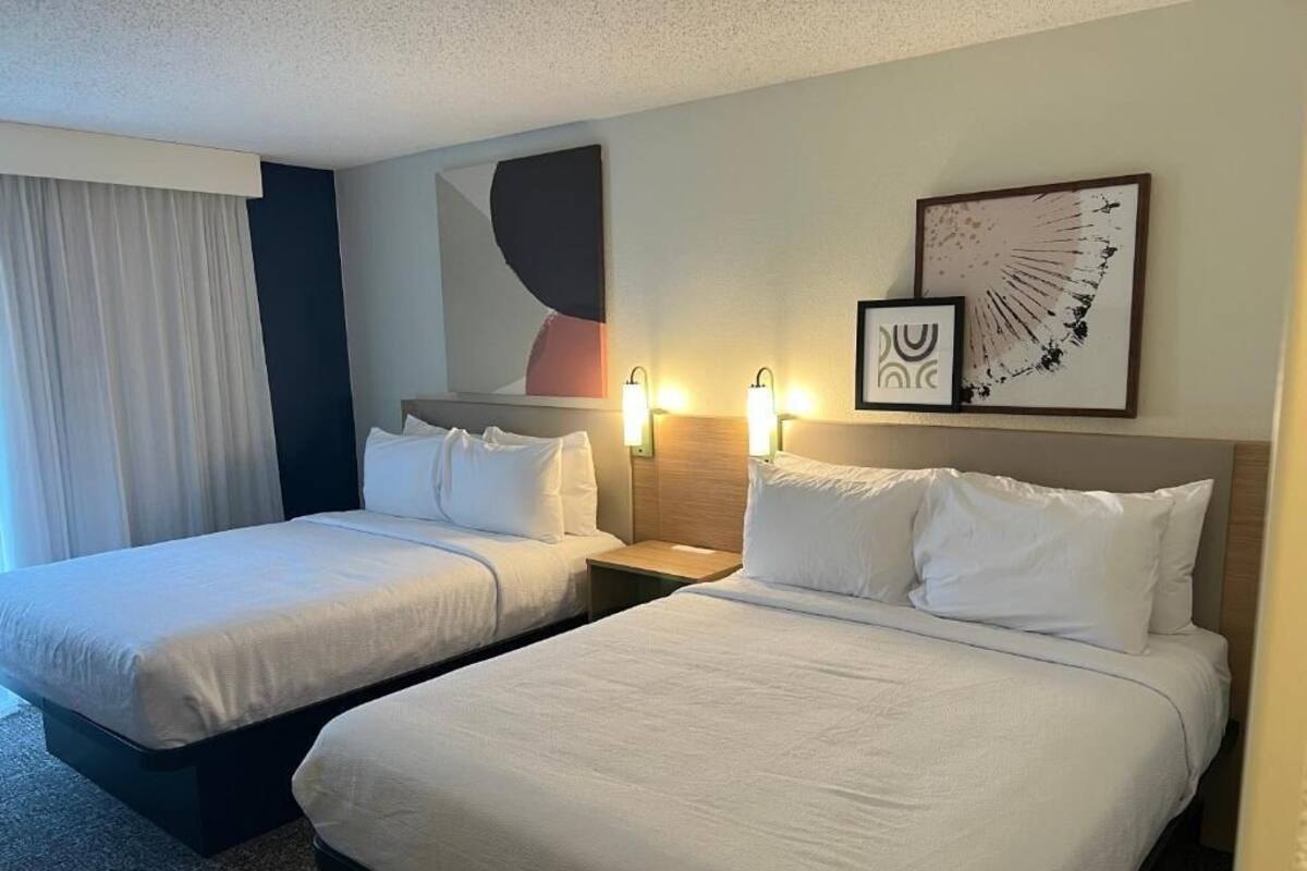 Een hotelkamer met twee bedden, een groot raam met gordijnen, decoratie aan de muur en bedlampjes.