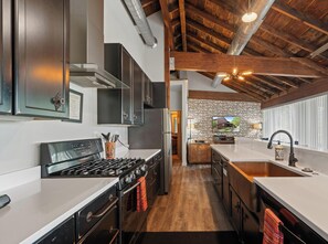 A modern kitchen with a large stove, dark cabinets, and a stone accent wall. - The Downtowner|Group & Event Friendly Space| 9BR Funhub Downtown Lake Geneva|Walk to Lake & Dining (Lake Geneva)