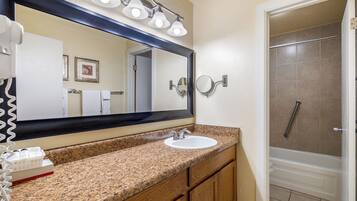 A bathroom with a granite countertop, white sink, and a large mirror. There is a shower area visible to the right.