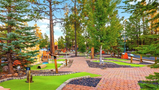Un campo de mini golf con un camino de ladrillo, césped verde y varios obstáculos.