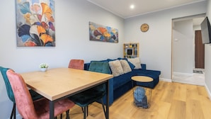 A modern living room with a wooden dining table, colorful chairs, a blue sofa, and abstract paintings on the walls. - Spodek Citylight Apartment (Katowice)