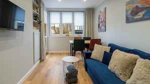 A modern living room with a blue sofa, a round coffee table, and a TV mounted on the wall. - Spodek Citylight Apartment (Katowice)