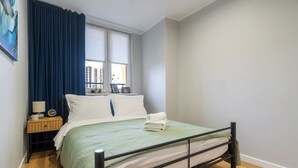 A neatly arranged bedroom with a bed, a nightstand, a lamp, and a window with curtains. - Spodek Citylight Apartment (Katowice)
