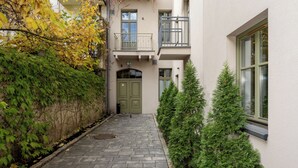 A paved courtyard with a green door, a small tree, and a building with a balcony. - Kraków Grzegórzki Deluxe Studio (Kraków)
