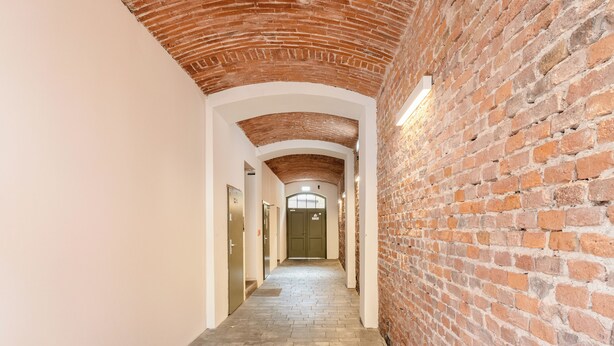 A corridor with brick walls and white arches, leading to a door at the end. - Kraków Grzegórzki Deluxe Studio (Kraków)