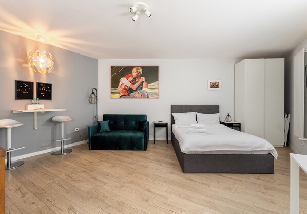 A modern bedroom with a bed, a green sofa, a desk with two chairs, a globe light, and a painting on the wall. - Kraków Grzegórzki Deluxe Studio (Kraków)