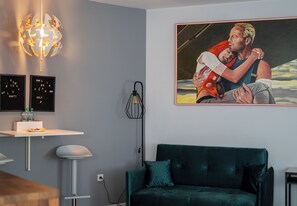 A modern living room with a green sofa, a globe light fixture, a painting, and a small table with bottles. - Kraków Grzegórzki Deluxe Studio (Kraków)