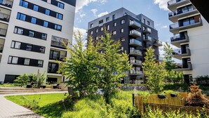 Un immeuble d’appartements moderne doté de nombreux balcons, d’un jardin bien entretenu et offrant une vue sur un ciel dégagé.
