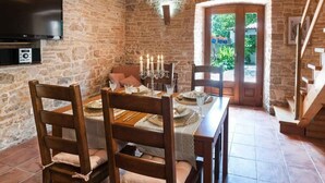 Uma sala de jantar com paredes de pedra, mesa posta para quatro pessoas, televisão na parede e escada que dá para uma área externa.