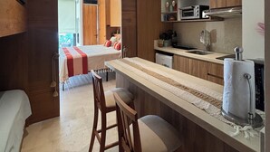 Cozinha compacta com armários de madeira, micro-ondas e forno embutido. Há um balcão com banquetas e uma grande janela com vista para o exterior.