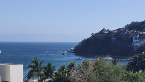 Vista costeira com céu claro, margem rochosa e edifícios numa encosta.