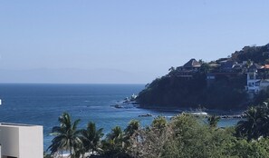 Vista costera con cielo despejado, costa rocosa y edificios en una ladera.
