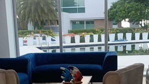 Een moderne hotelkamer met een groot raam, een blauwe bank, twee fauteuils en een bijzettafeltje met decoratieve voorwerpen.