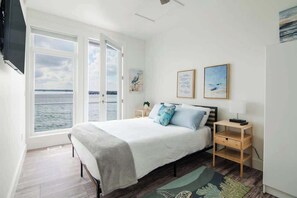 A bedroom with a bed, two bedside tables, a window with a view of the sea, and two framed artworks on the wall. - Chic Lakefront Getaway W/ Hot tub + Kayaks! (Alanson)