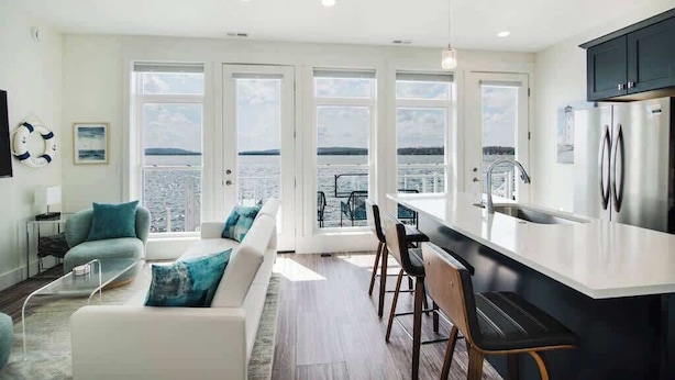 A modern kitchen with a large island, white cabinetry, and a view of the sea through large windows. - Chic Lakefront Getaway W/ Hot tub + Kayaks! (Alanson)