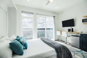 Una habitación de hotel moderna con una cama grande, televisión, escritorio y vista al agua.