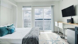 A hotel room with a bed, a desk, a television, and a view of the sea. - Chic Lakefront Getaway W/ Hot tub + Kayaks! (Alanson)