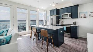 A modern kitchen with dark cabinets, stainless steel appliances, and a large island with bar stools. - Chic Lakefront Getaway W/ Hot tub + Kayaks! (Alanson)