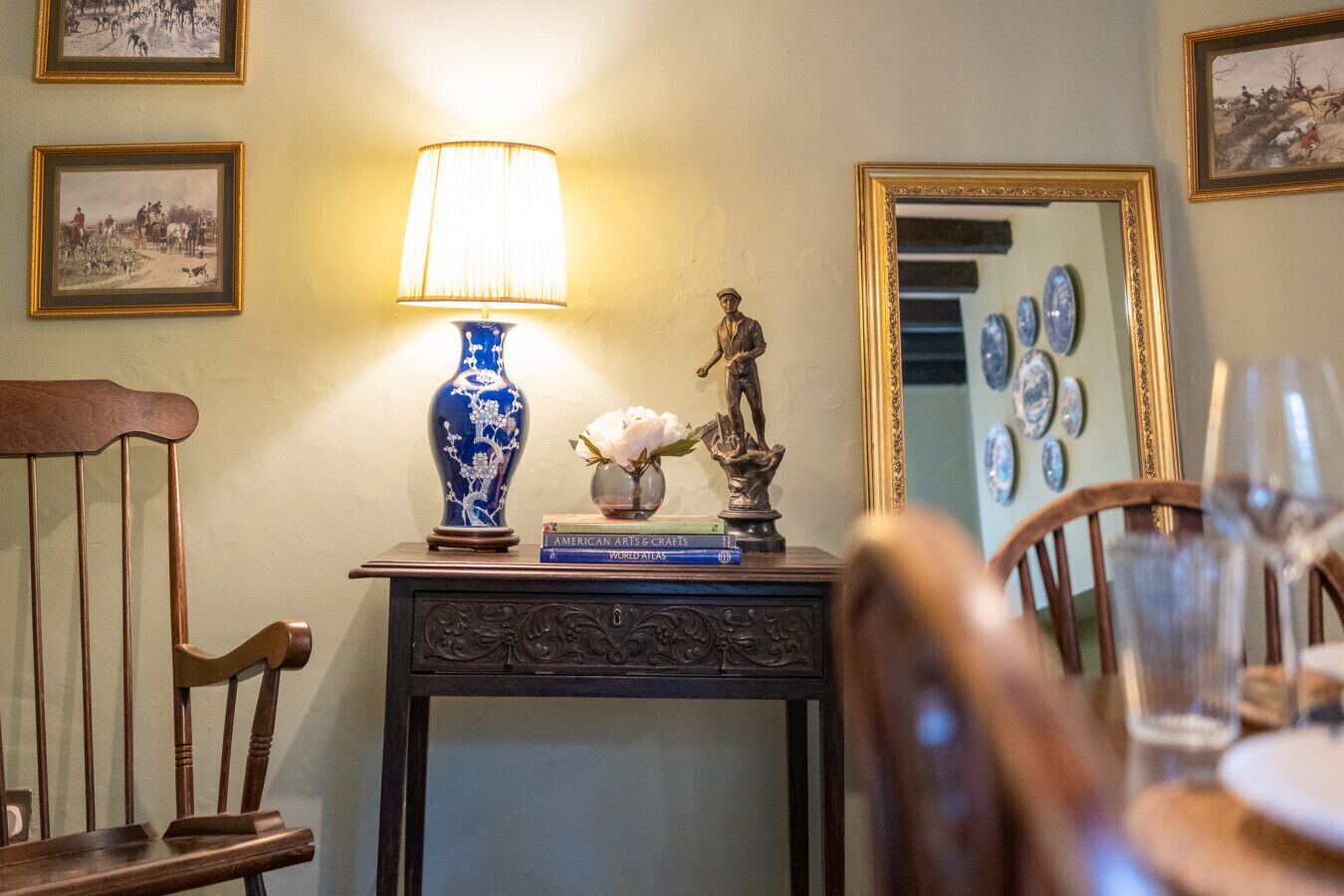 A dining area with a table set for two, a blue vase, a statue, and framed pictures on the wall.