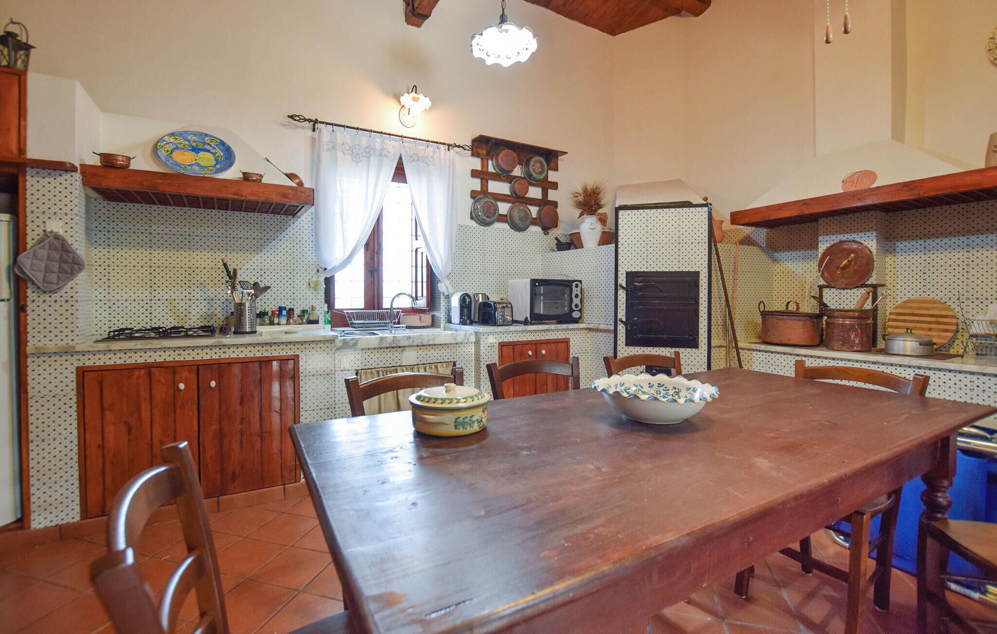 Una cocina con una mesa de madera, sillas, estufa, microondas y distintos utensilios de cocina.