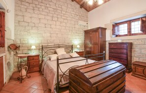 A bedroom with a stone wall, a wooden bed, a dresser, and a window with wooden shutters. - Lovely home in Modica (Modica)