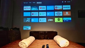 A hotel room with a bed, two remote controls, and a wall-mounted screen displaying various app icons. - Hostal Tres Reyes (Cusco)