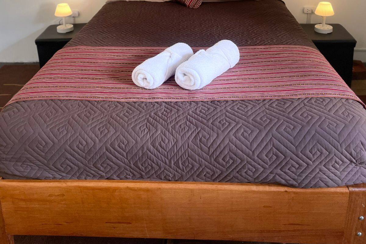 Een opgemaakt bed met een bedsprei met dessin, twee opgerolde handdoeken, een houten hoofdbord en bedlampjes.