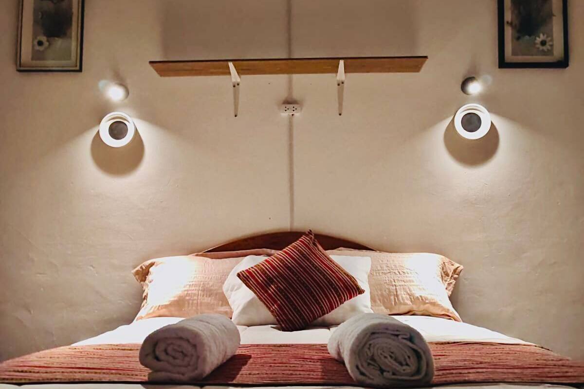 Een net opgemaakt bed met opgerolde handdoeken, een houten plank erboven en twee wandlampen.
