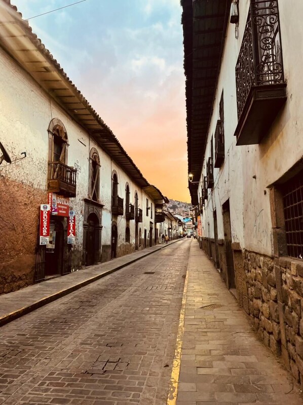 A narrow cobblestone street flanked by old buildings with balconies and signage for local businesses. - Alojamiento en Casona Colonial Céntrica (Cusco)