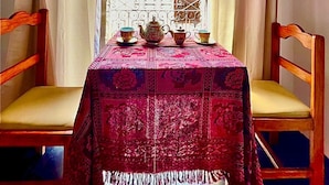 A room with a table set for tea, two chairs, a window with curtains, and a view of a building outside. - Hostal Tres Reyes (Cusco)