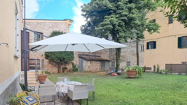 Terrassa exterior amb taula i cadires, un parasol gran i un camí de pedra.