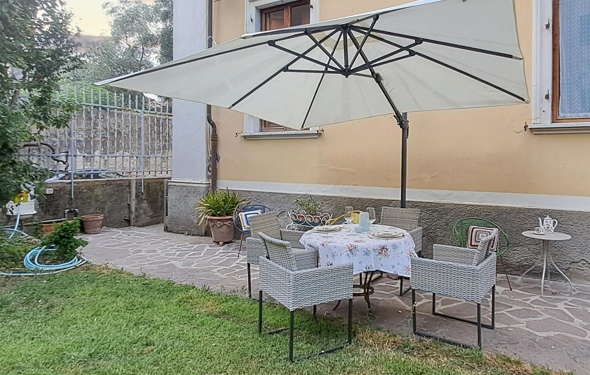 An outdoor patio with a table set for two, surrounded by wicker chairs, under a large umbrella.