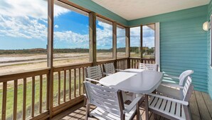 A covered outdoor seating area with a table and chairs, overlooking a beach and marshy landscape.
