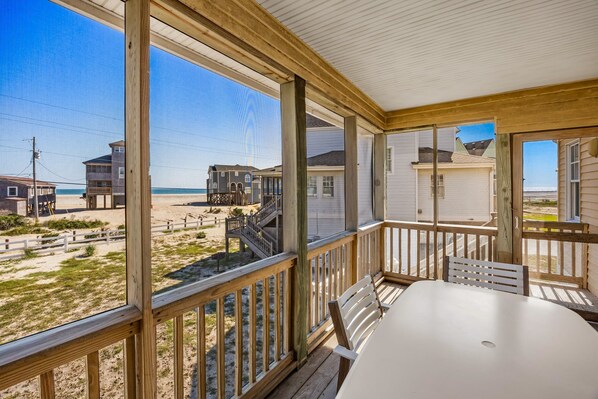 A covered outdoor area with a view of the beach, wooden deck, and a table with chairs. - Egret – Bright Buxton Townhome w/ Ocean Views (Buxton)