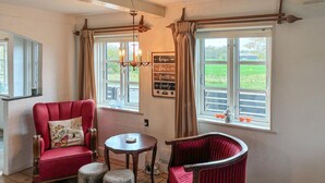 A cozy room with a red armchair, a small table, and two stools. There are two windows with curtains, a chandelier, and a sign on the wall. - Beautiful home in Stege with WiFi (Stege)