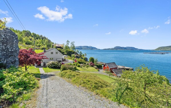 A coastal property with a gravel driveway leading to a white house with a red roof, surrounded by lush greenery and a view of the sea. - Cozy home in Skiftun with house sea view (Skiftun)