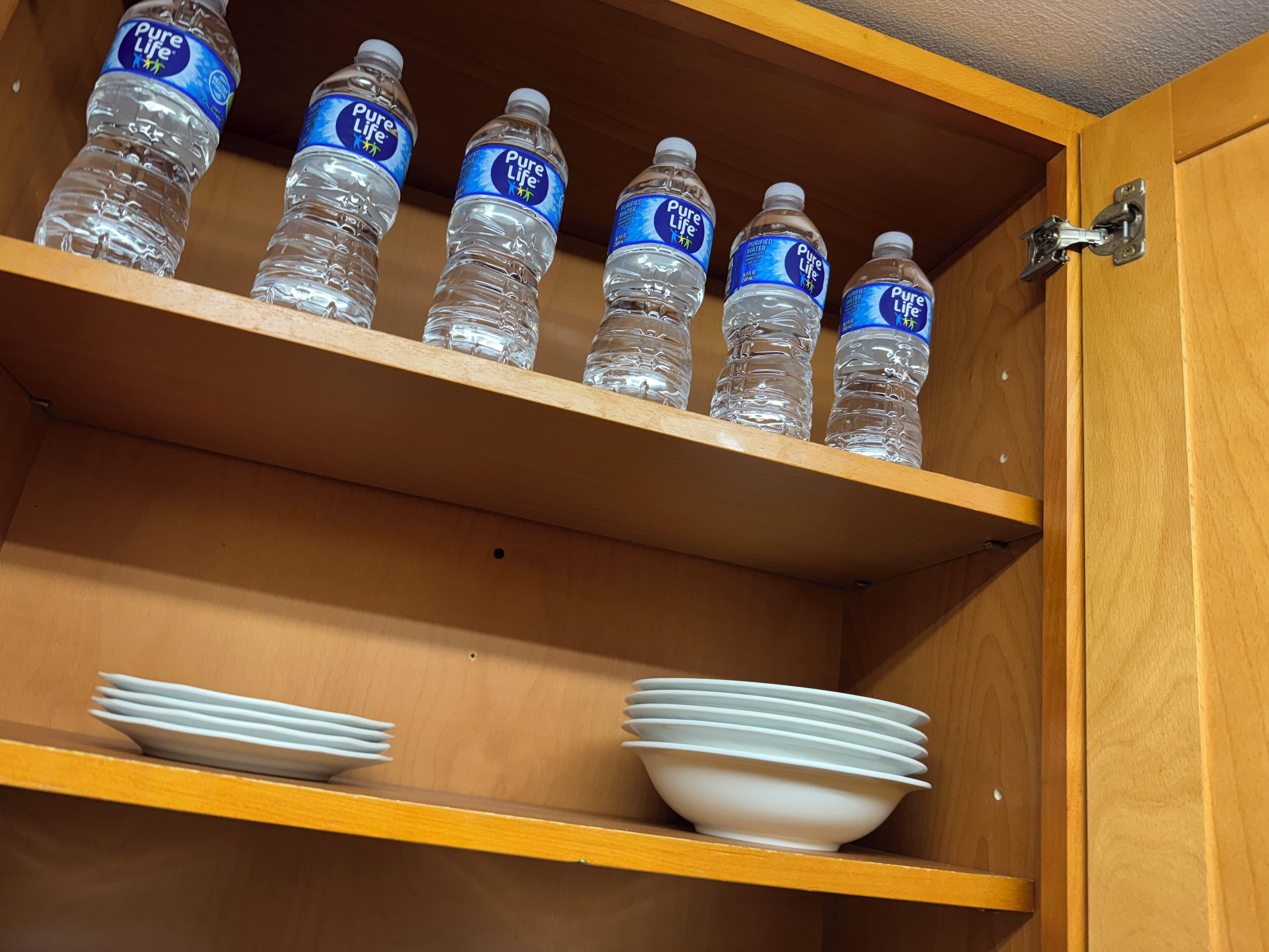 Un meuble en bois doté d’étagères où sont rangées des bouteilles d’eau et des assiettes blanches.