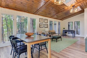 Une pièce spacieuse avec un plafond en bois, de grandes fenêtres, une table à manger avec des chaises, un canapé et une petite table sur laquelle se trouve un bol.