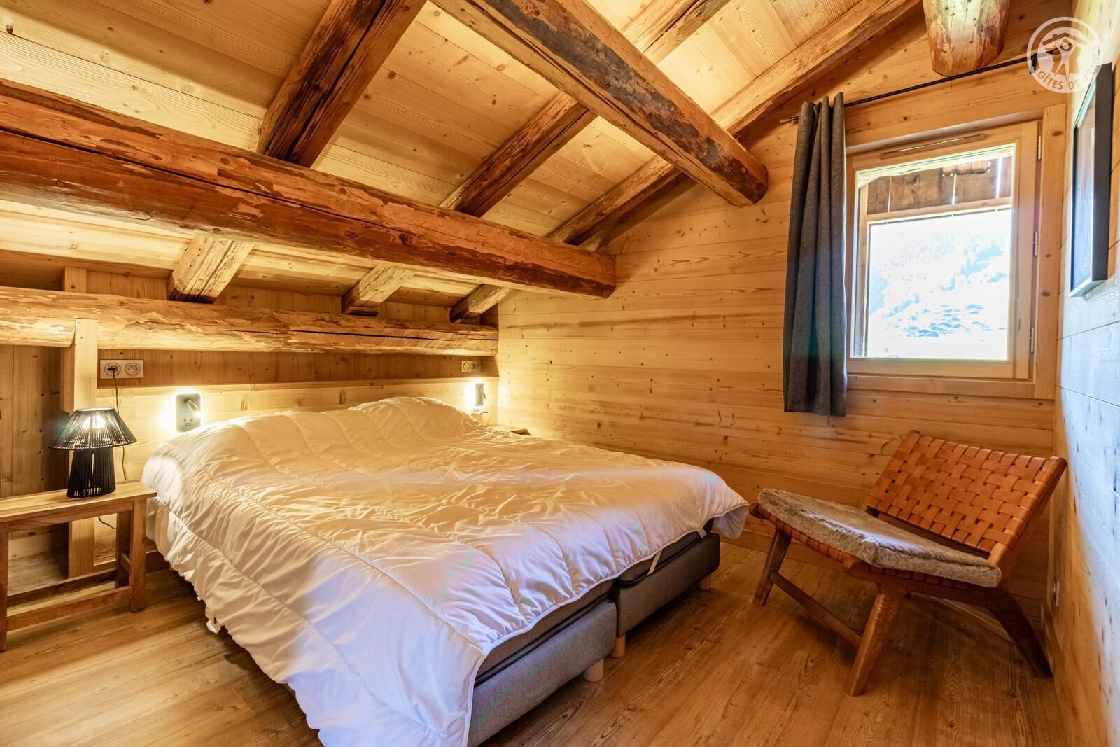 Un dormitorio rústico de madera con una cama, una lámpara de noche y una silla.