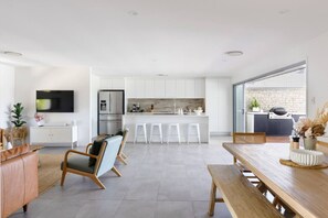 A modern kitchen with white cabinets, a built-in oven, and a dining area with a wooden table and bar stools. - Palm Beach Family Retreat (Palm Beach)