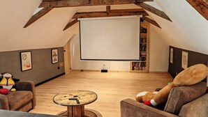 A cozy attic room with a wooden ceiling, a large white projection screen, a plush sofa with a teddy bear, a small round table, and a bookshelf filled with books. - Paradise lost swimming pool jacuzzi billiards table soccer... (Louvie-Juzon)