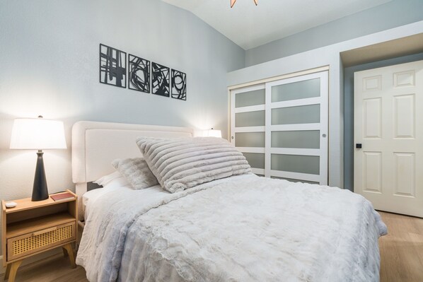 A bedroom with a bed, nightstand, lamp, and artwork on the wall.