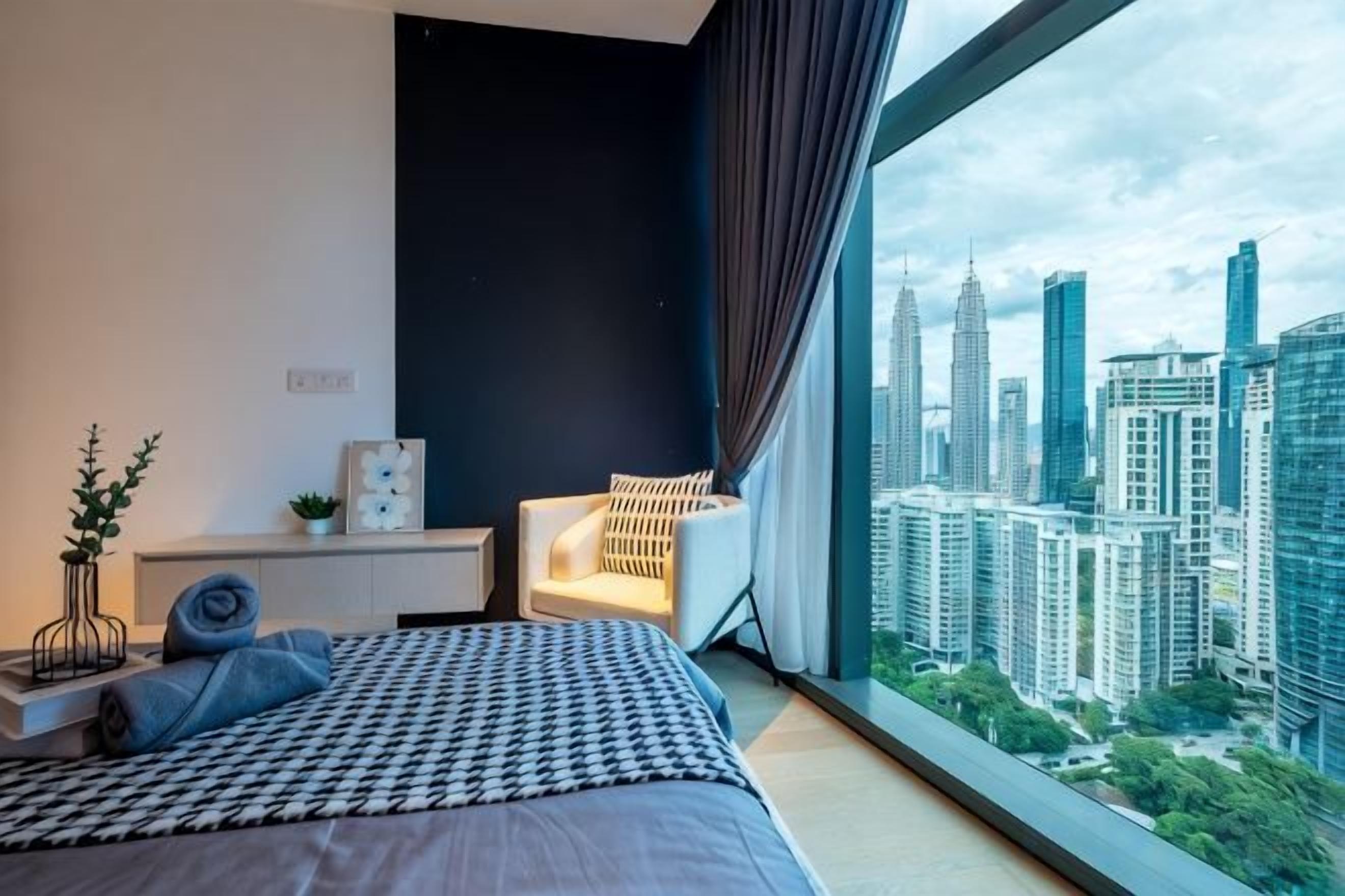 A modern bedroom with a large bed, a nightstand, a chair, and a city view through a large window.