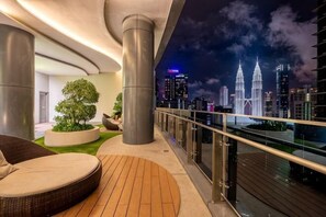 En balkon med udsigt over byens skyline, inklusive Petronas Towers, samt et siddeområde med et rundt bord og stole.