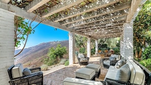 Un espace extérieur aménagé avec des meubles en osier, un pilier en pierre et une vue sur un paysage montagneux.