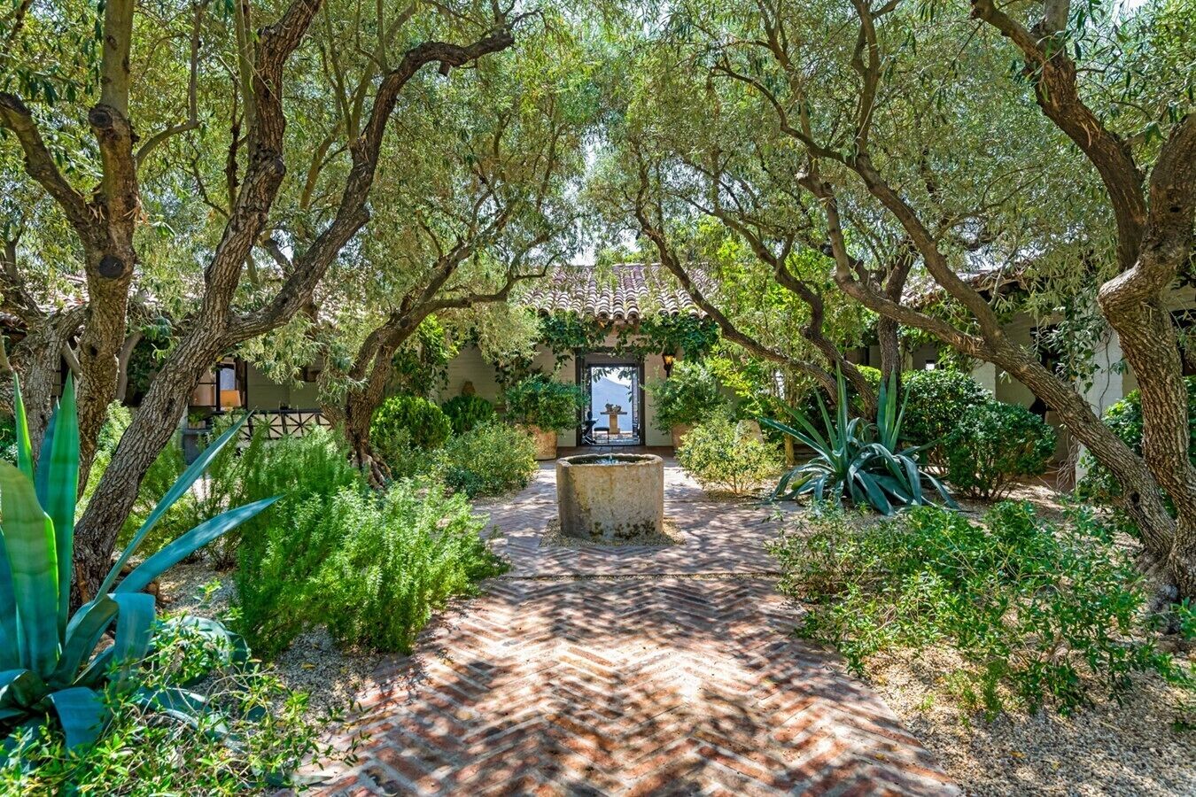 Un sentier de jardin mène à un belvédère agrémenté d’une fontaine, le tout étant entouré d’une végétation luxuriante et d’arbres.