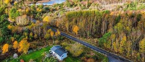 An aerial view of a rural area with a winding road, a small house, and a pond.