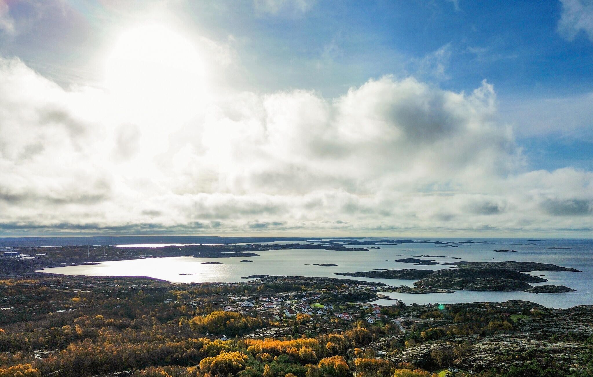 A coastal landscape with a view of a small town, a body of water, and a cloudy sky.