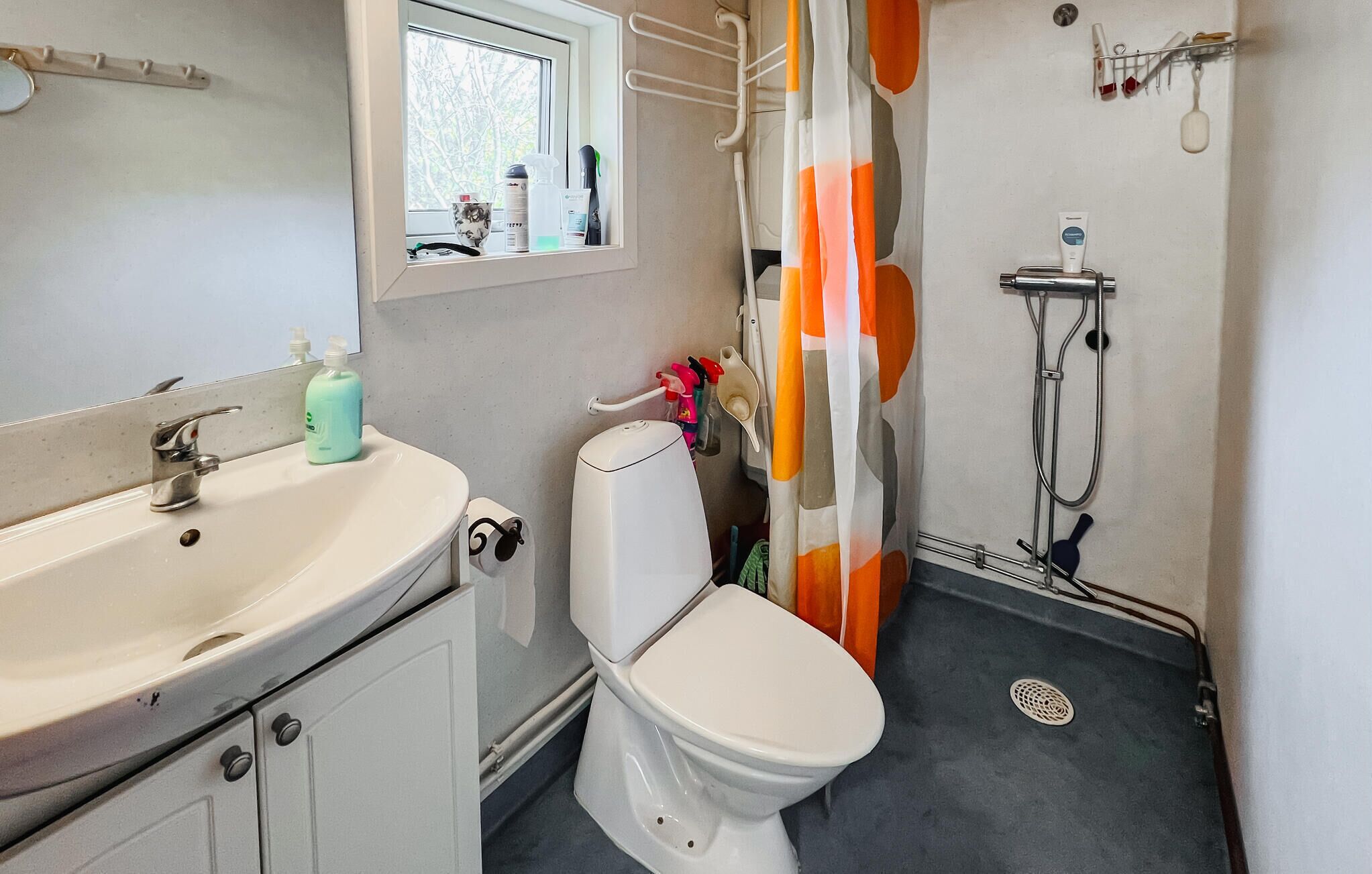A bathroom with a toilet, sink, shower, and a window.