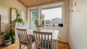 Un coin repas comprenant deux chaises en bois, une table blanche et une vue sur l’extérieur grâce à une grande fenêtre.